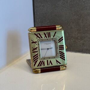 A gold and red Cartier travel size alarm clock. Roman numerals on the bezel.